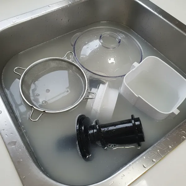 Disassembled juicer parts soaking in a natural cleaning solution for mold removal