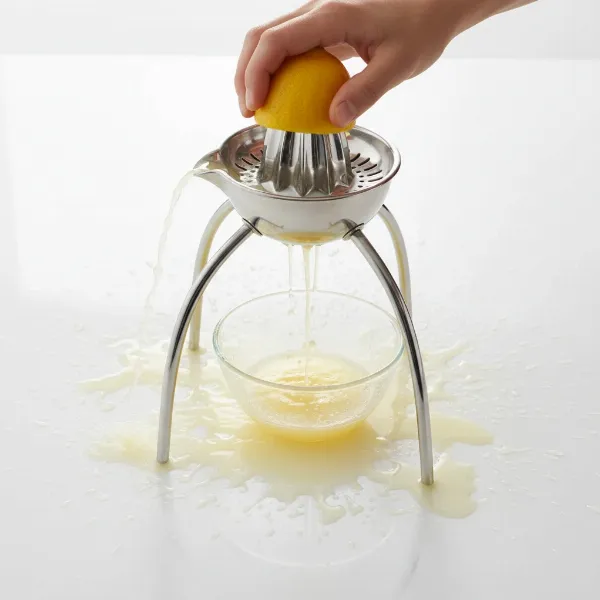 A lemon being juiced on an Alessi Juicy Salif, showing juice dripping onto the counter and hands.
