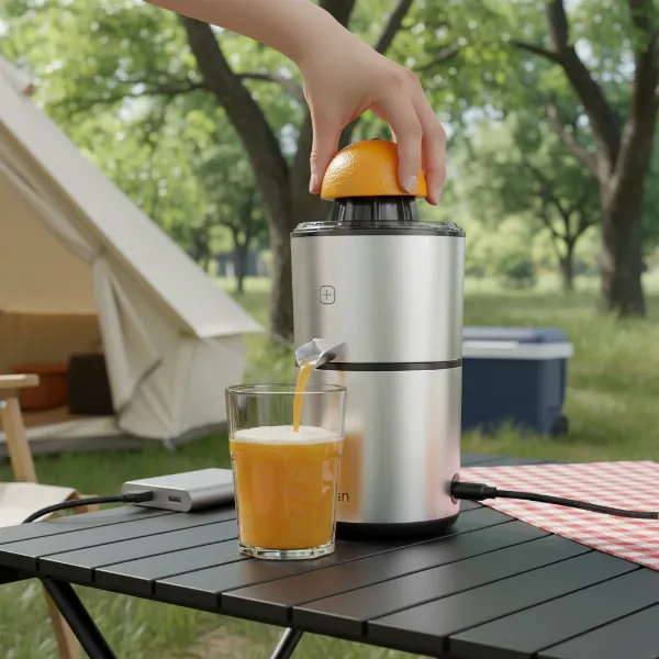 A person using a compact, rechargeable USB-C electric citrus juicer outdoors, making fresh orange juice.
